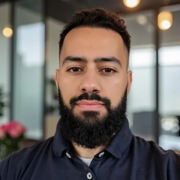 Porträt von Ahmed Mowafek: Mann mit Vollbart im dunkelblauen Poloshirt, dahinter ein heller Raum.